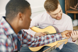 Dois adultos com guitarras durante uma explicação da posição da mão no instrumento