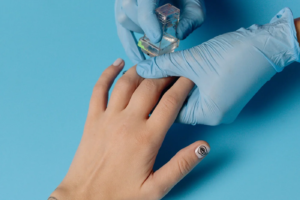 Aplicação de produto nas unhas por uma pessoa com luvas azuis