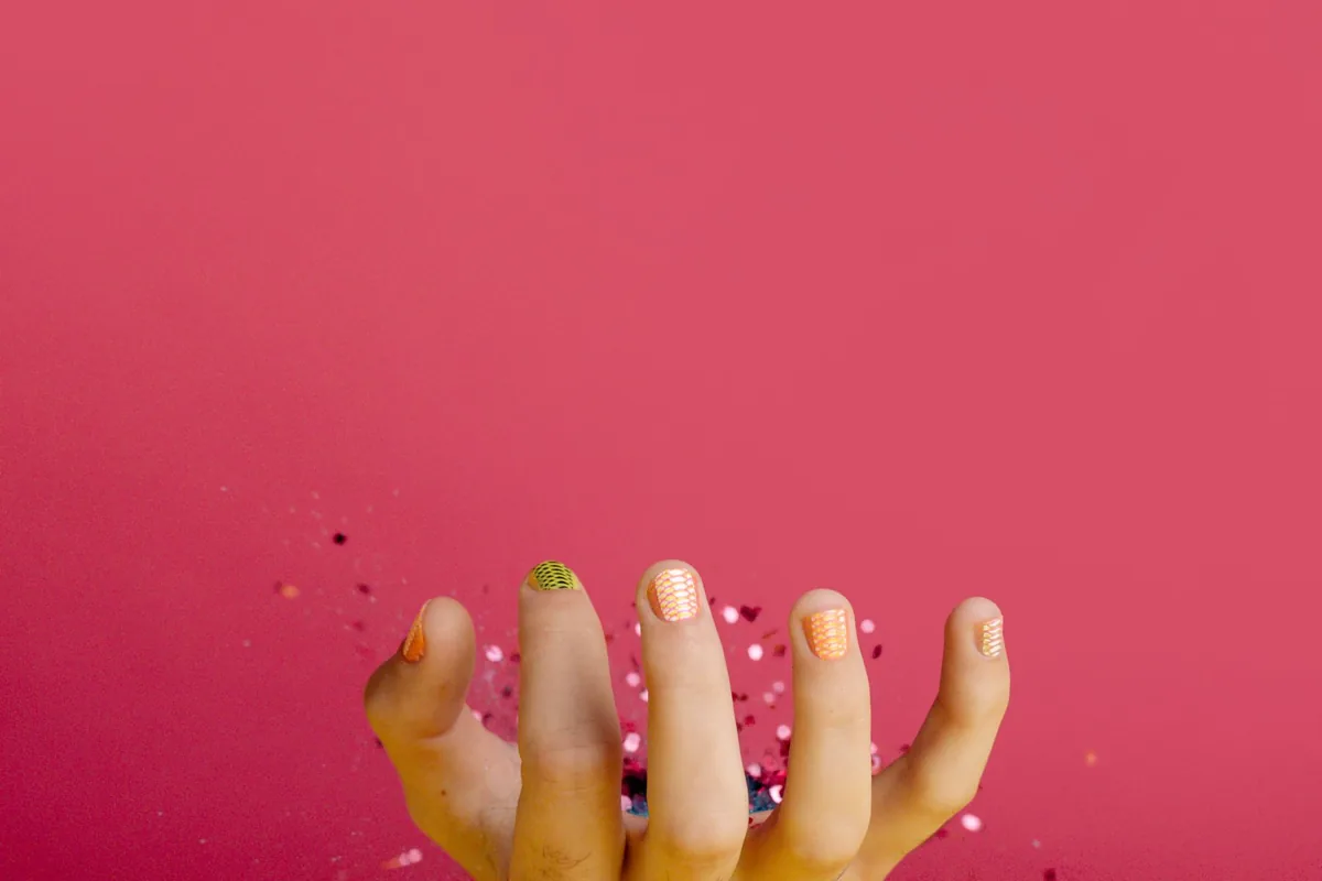 Mão com unhas decoradas em cores vivas sobre fundo rosa